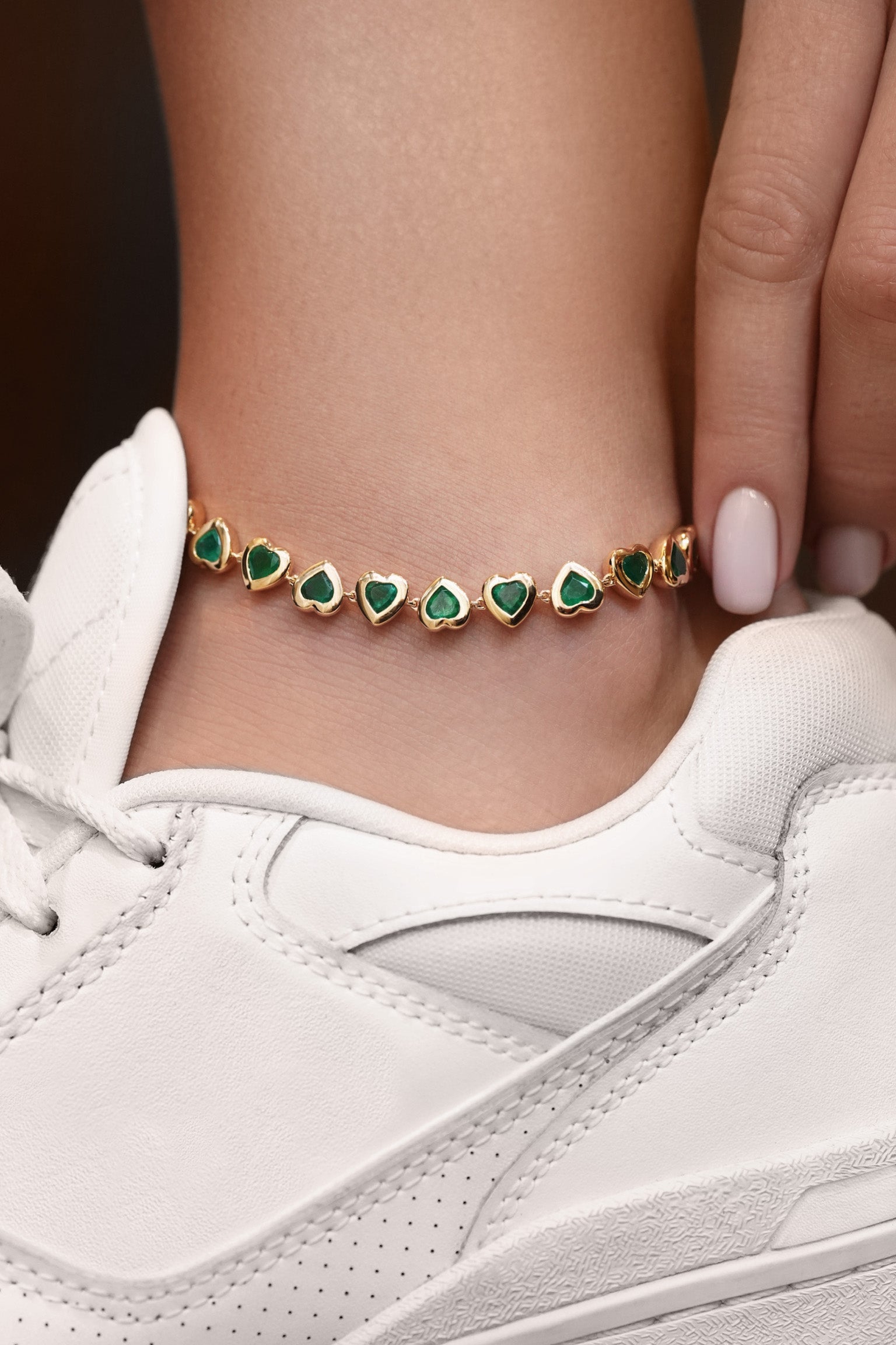 Close-up of a person wearing a gold bracelet with green gemstones on a white sneaker.