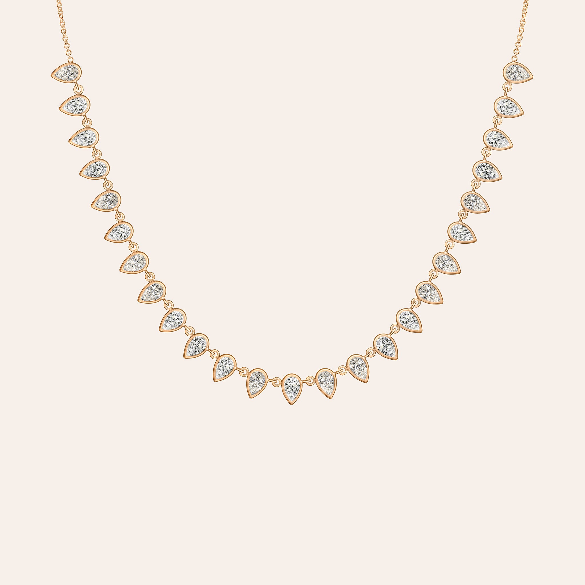 The Lena Pear Shape Necklace in 14K rose gold, with a fringe of bezel-set pear-shaped diamonds, shown against a cream background.