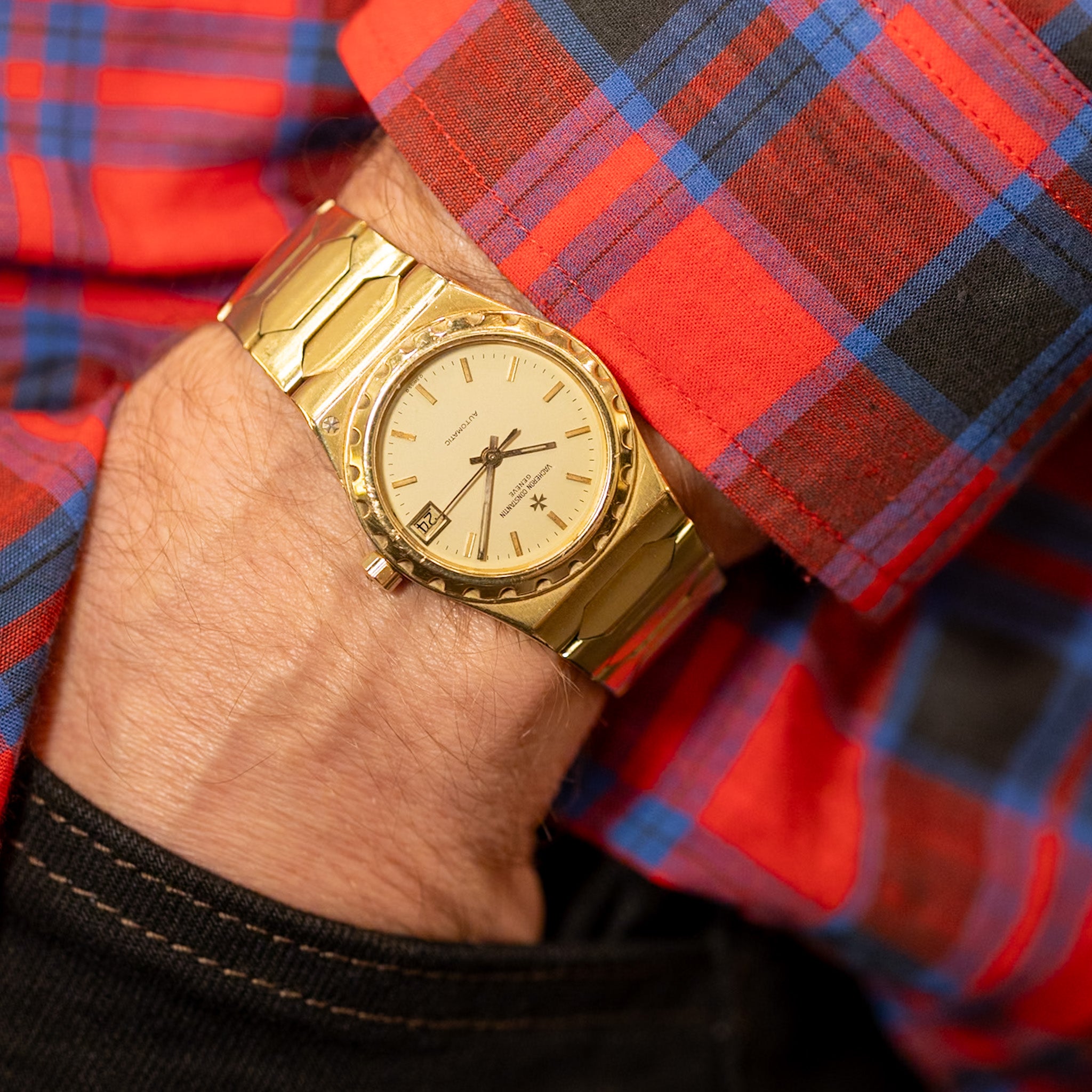 Gold wristwatch on a person's hand with a red and blue plaid shirt in the background