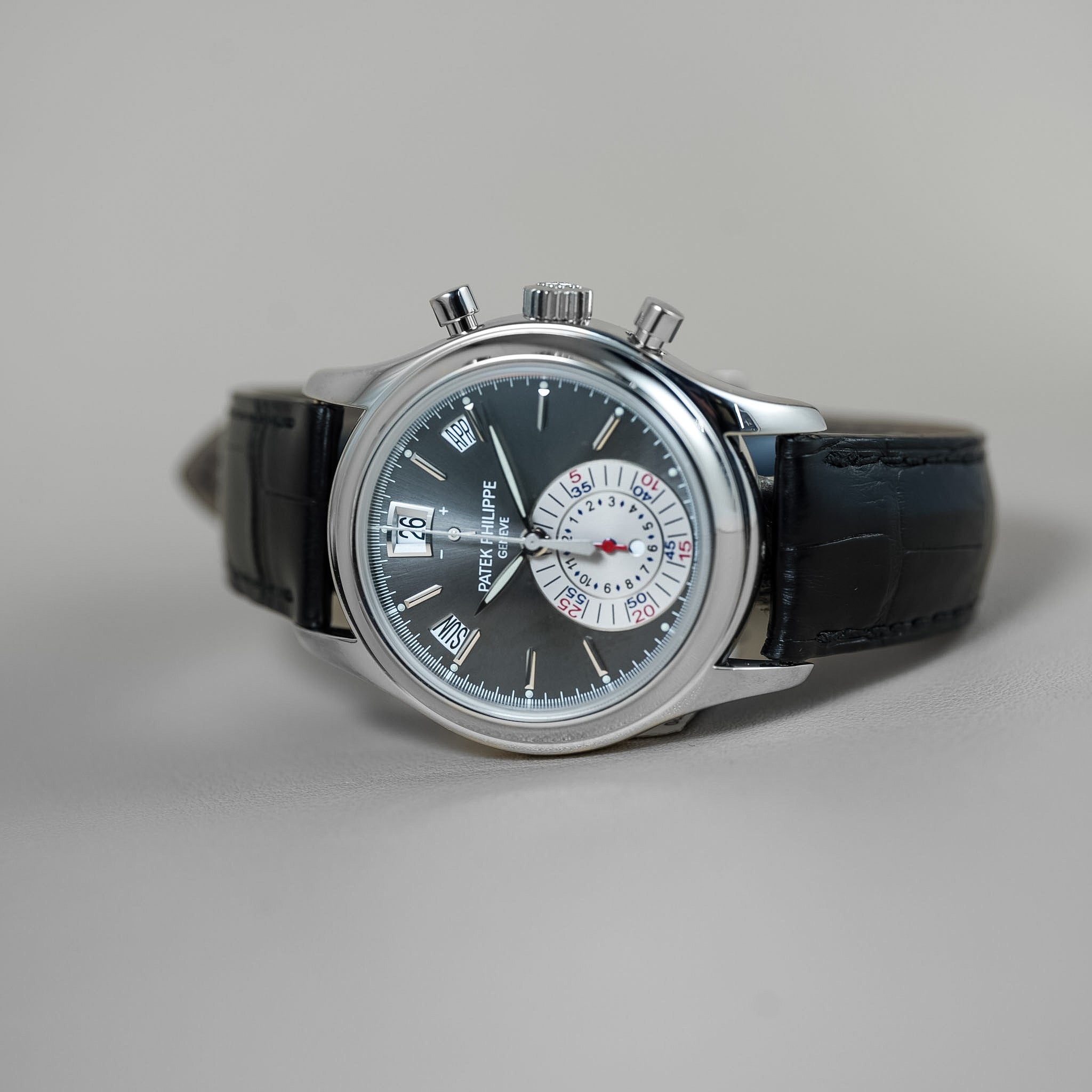 Luxury watch with black leather strap and silver case on a gray background