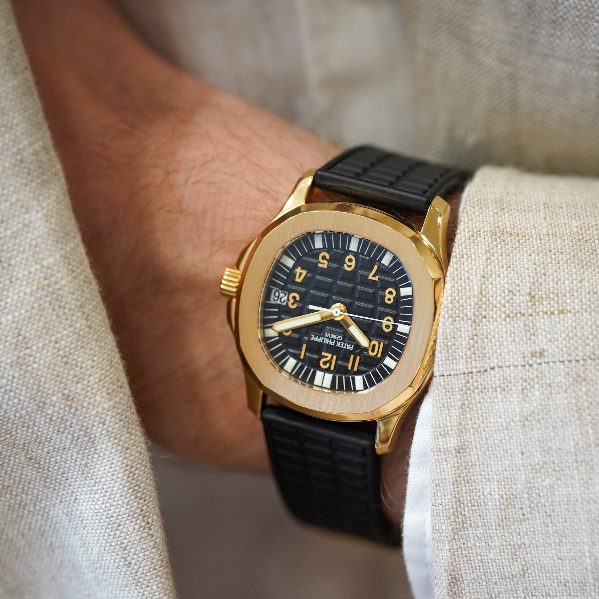 Gold watch on-wrist of a man wearing a tan jacket