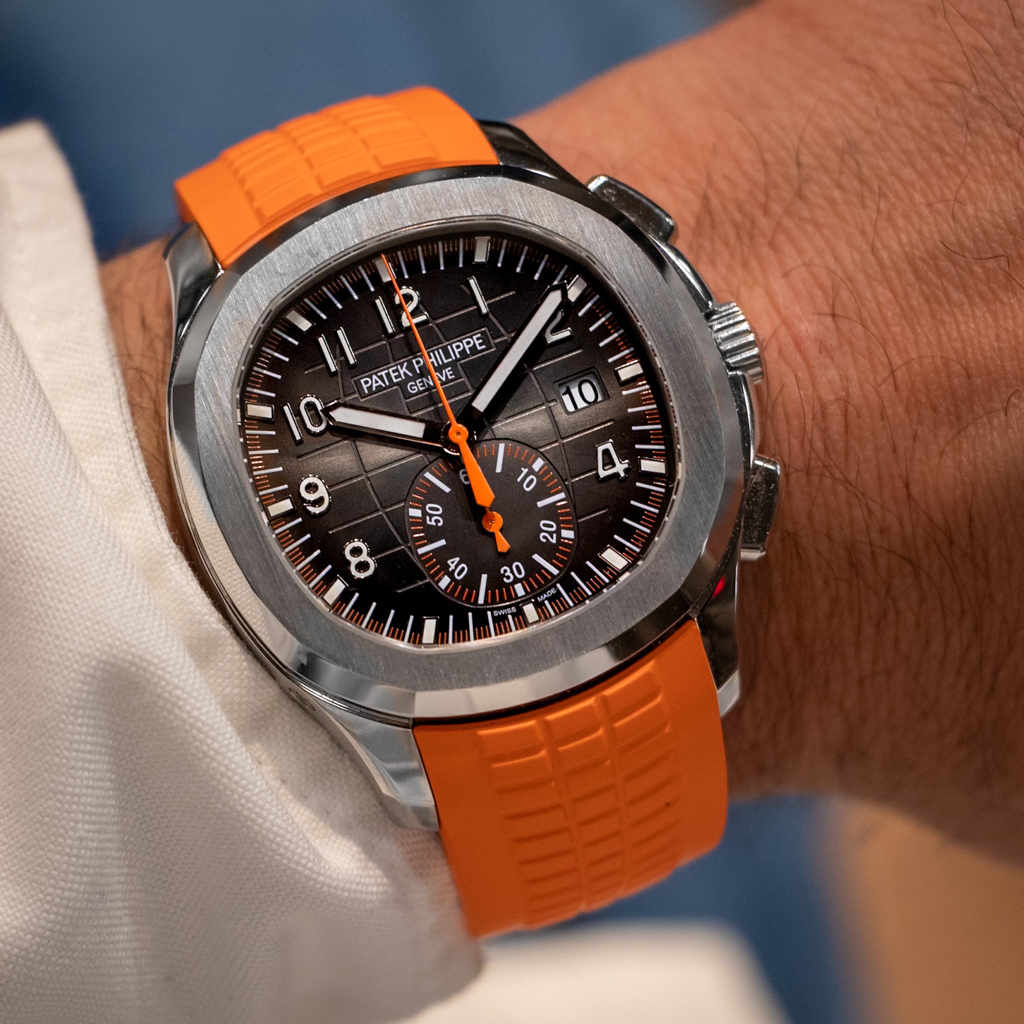 Watch with orange strap and black dial on a wrist, brand visible