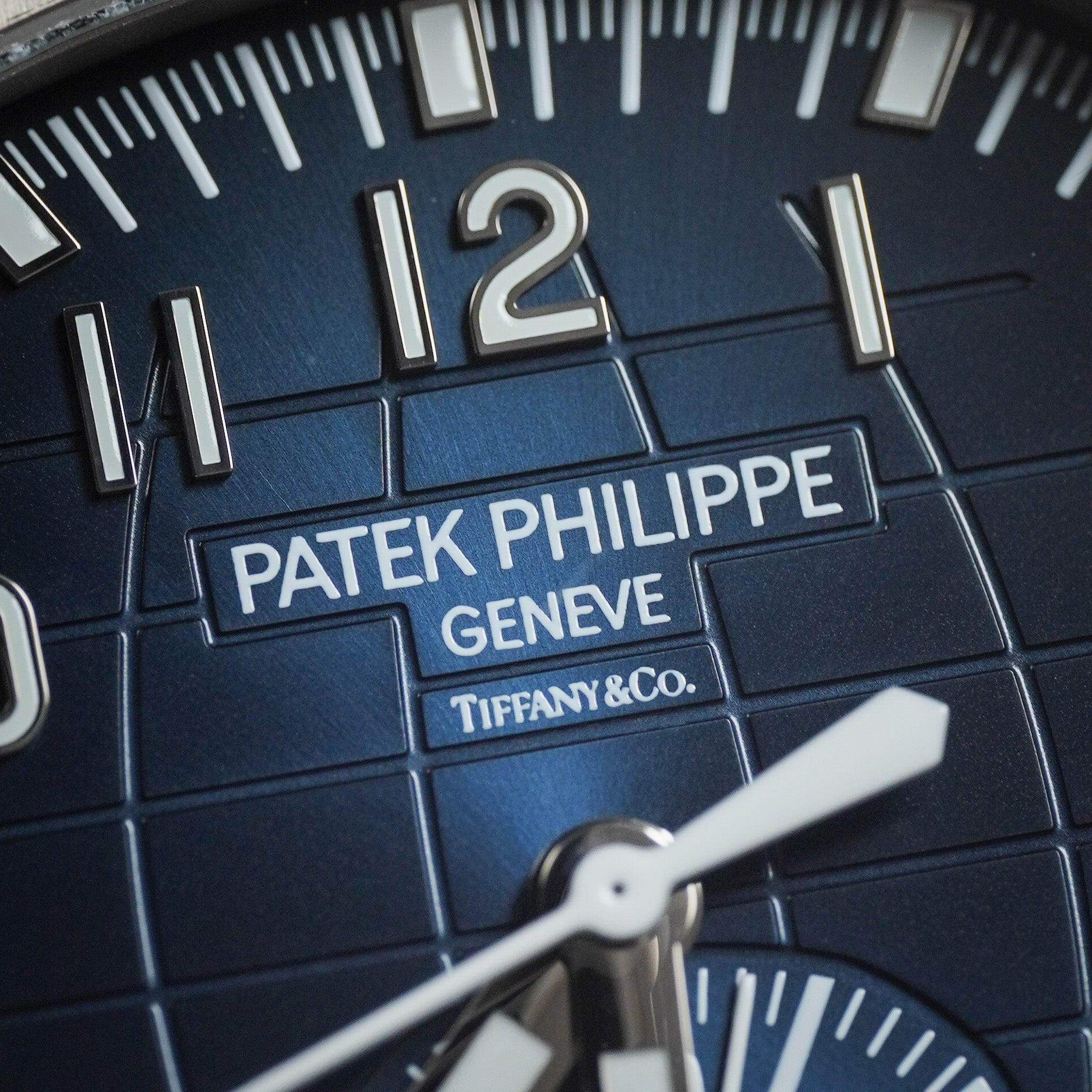Close-up of a Patek Philippe Geneve x Tiffany & Co. watch dial, featuring a dark blue textured background with silver-tone numerals and hands, and the brand logos clearly visible.