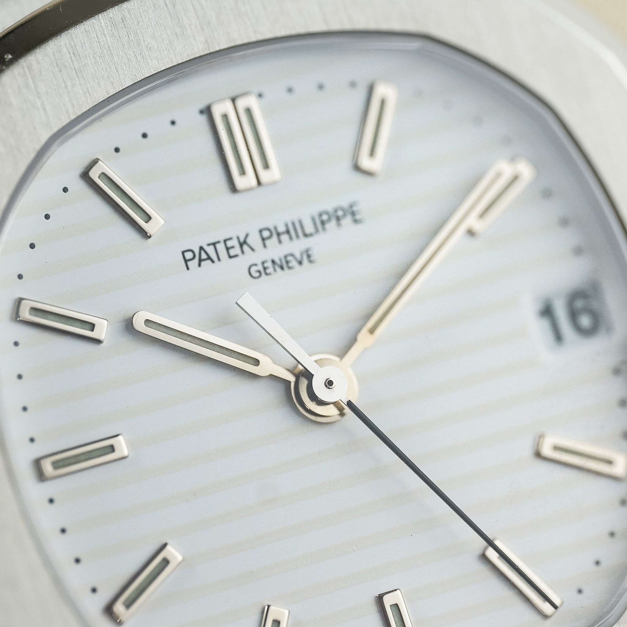 Close-up of a Patek Philippe Geneve watch dial with a silver-toned brushed metal case, white sunburst dial, and silver hour markers.