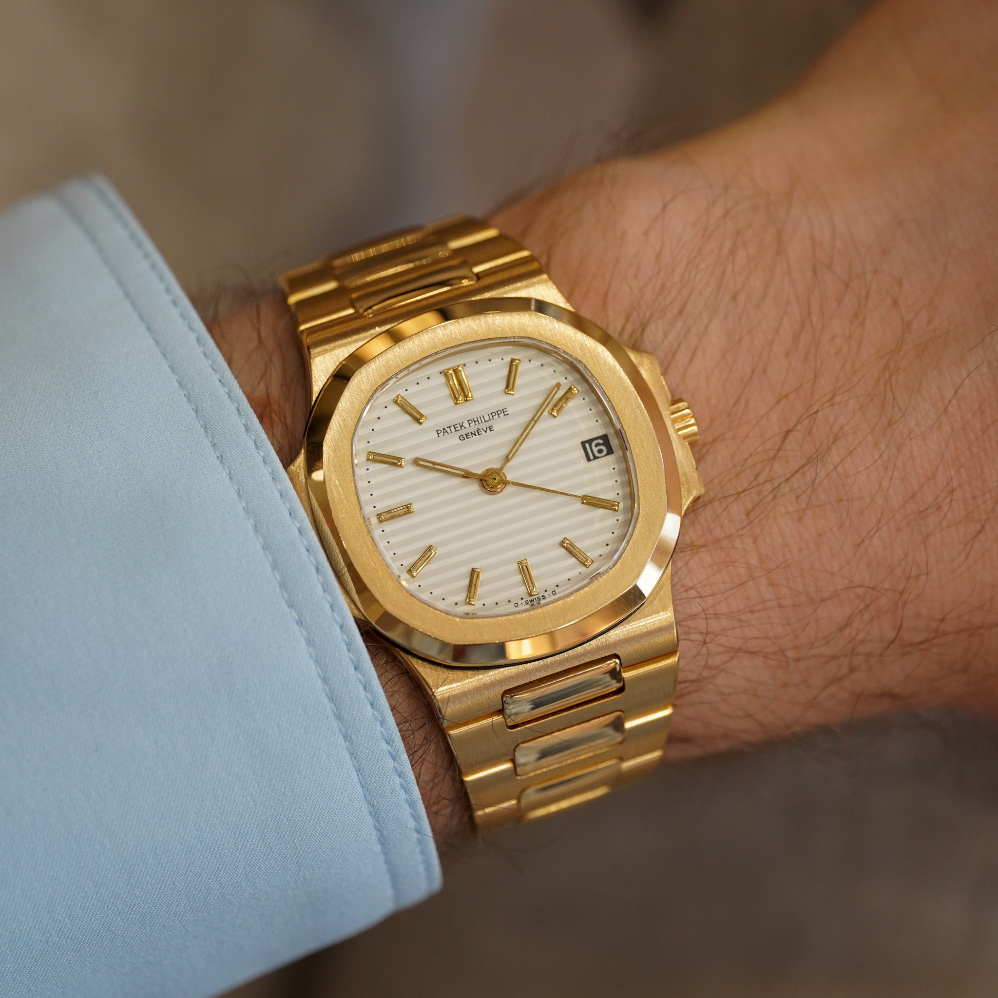 Gold wristwatch on a person's wrist with a light blue sleeve.