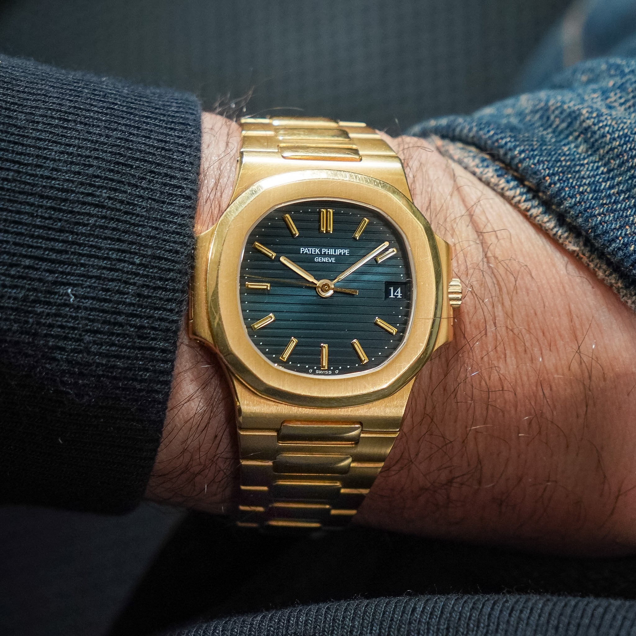 Gold watch with a blue face on a wrist, worn with denim jeans.