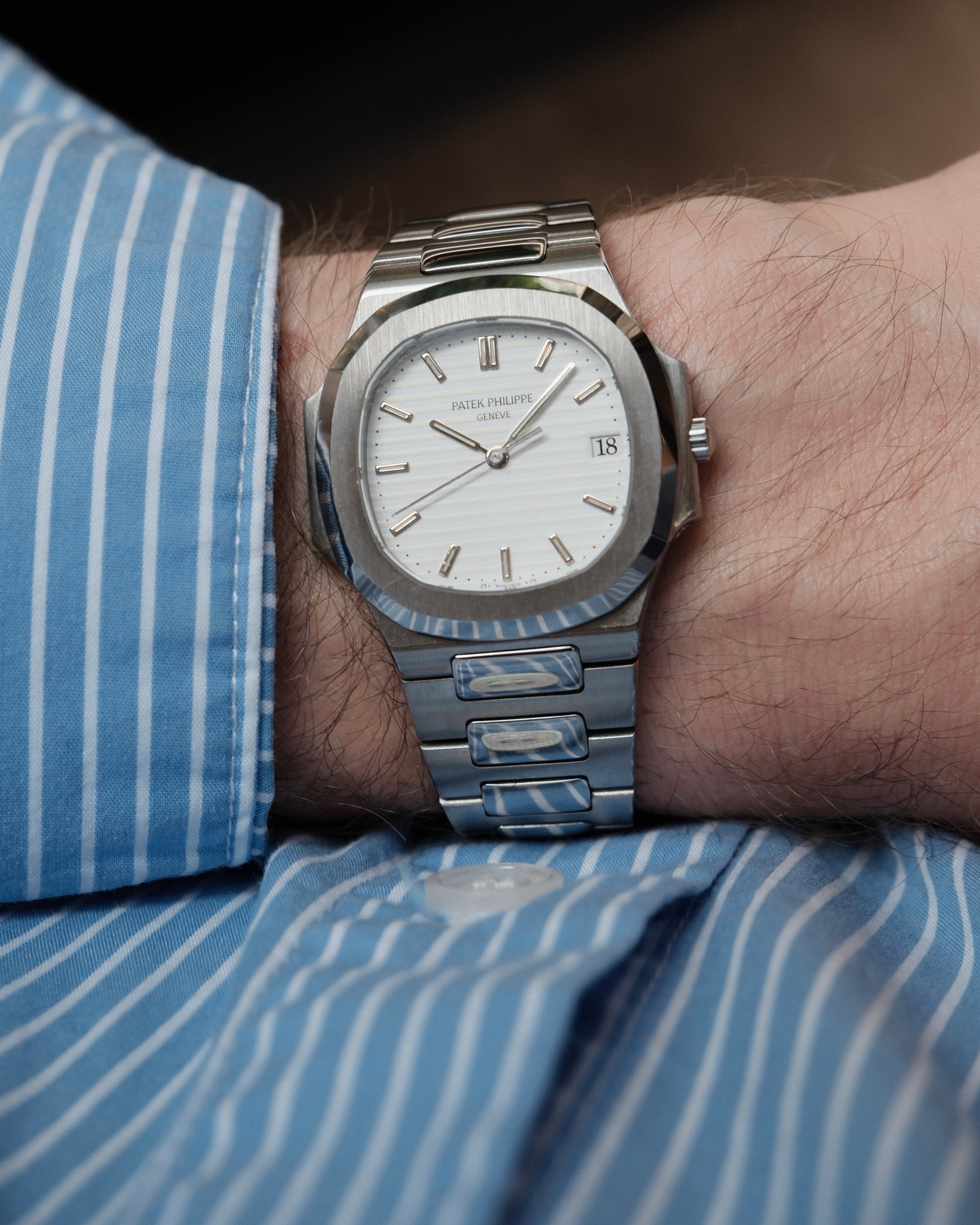Steel watch with a white dial on a man's wrist wearing a blue striped shirt