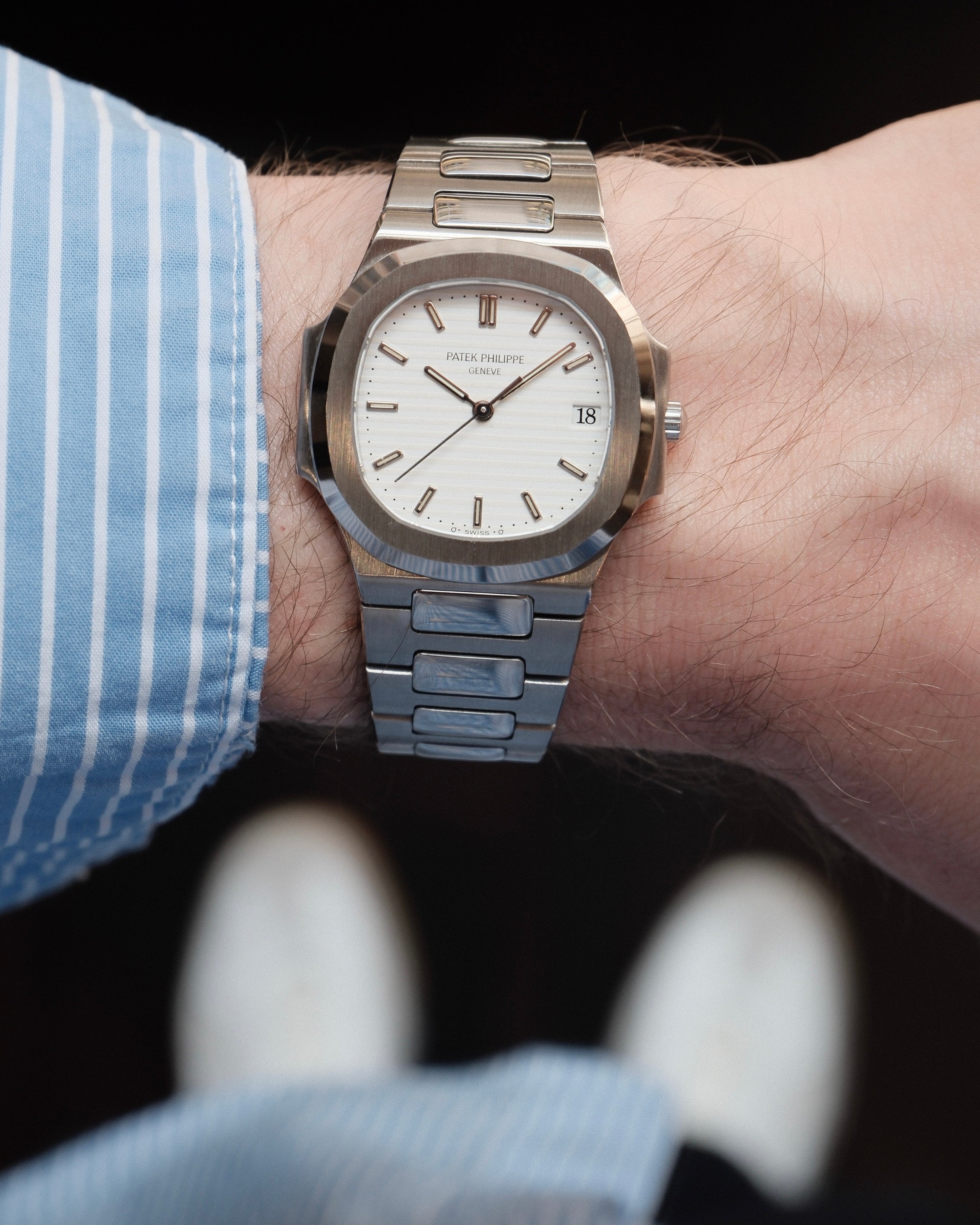 A silver-toned stainless steel wristwatch with a white dial and date window, worn on a person's wrist. The watch has a matching metal link bracelet and a fluted bezel.