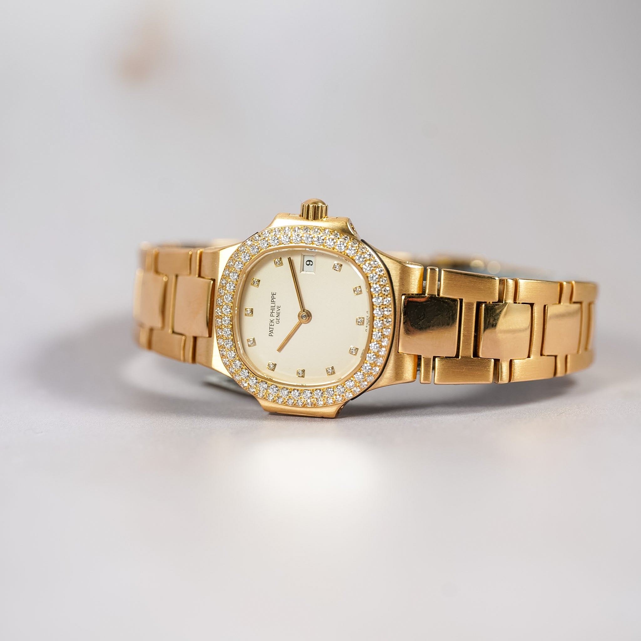 Gold wristwatch with diamond-studded bezel on a light gray background