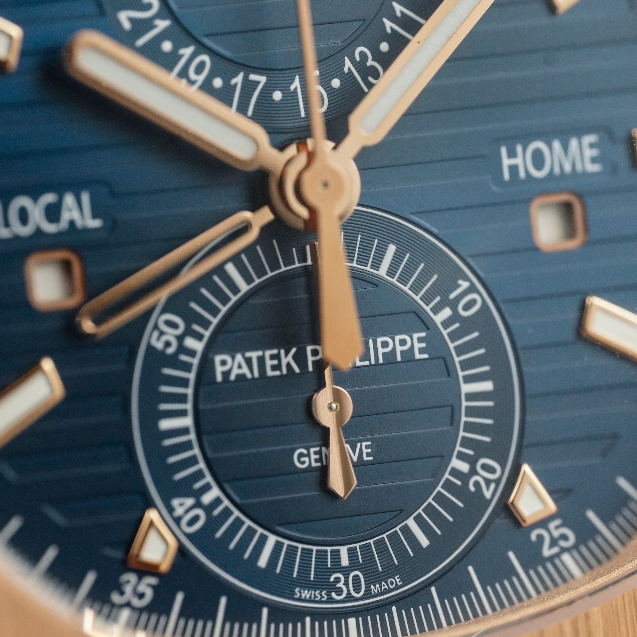 Close-up of a Patek Philippe watch face with gold accents on a blue background.