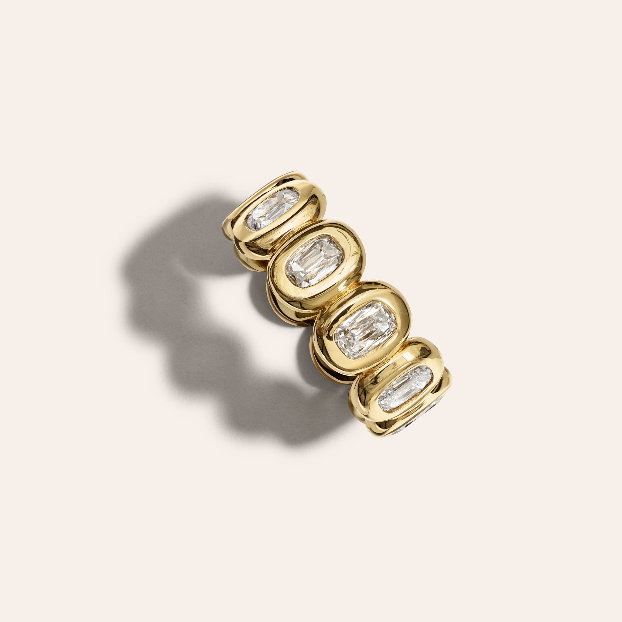 Retrouvai Antique Cushion Diamond Bezel Eternity Band in 18K yellow gold, with bezel-set antique cushion diamonds circling the band, shown against a dark background.