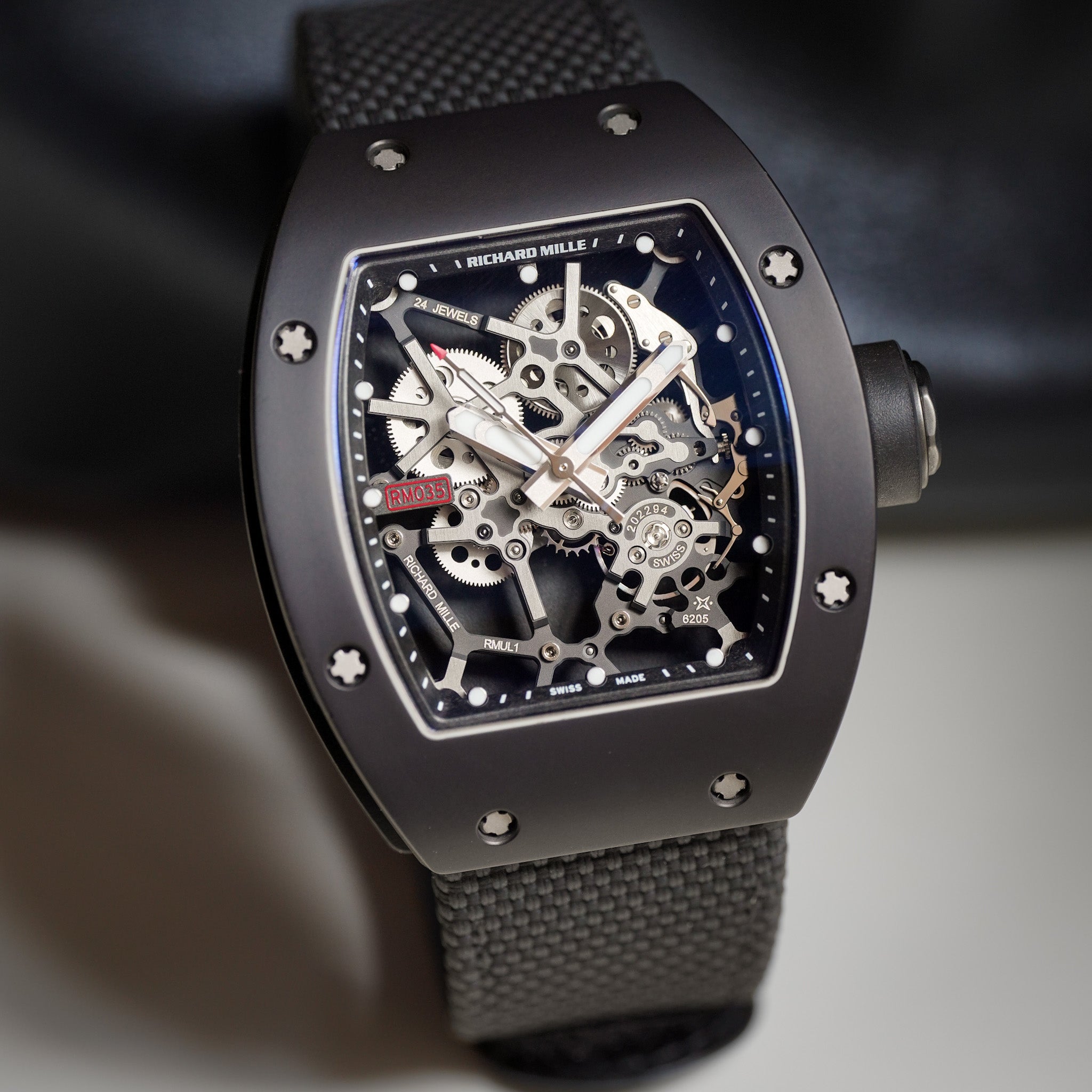 Richard Mille wristwatch with a dark gray carbon fiber case, skeletonized dial showing intricate silver gears, and a textured dark gray strap.