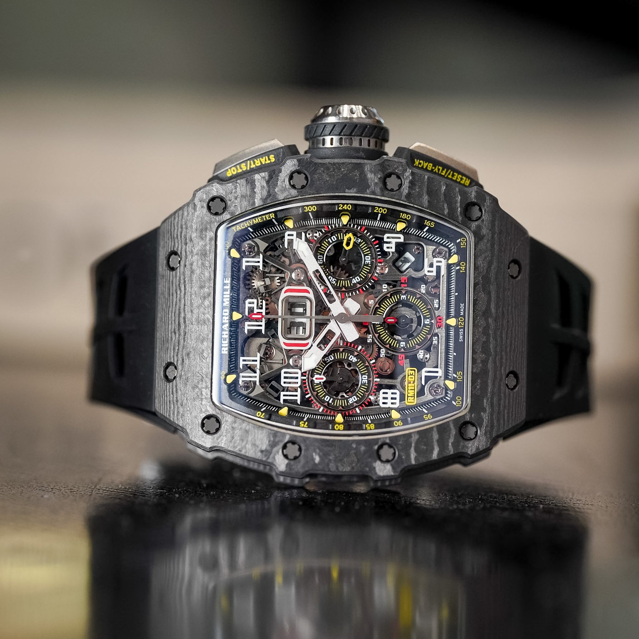 Luxury watch with detailed face and carbon fiber strap on a reflective surface
