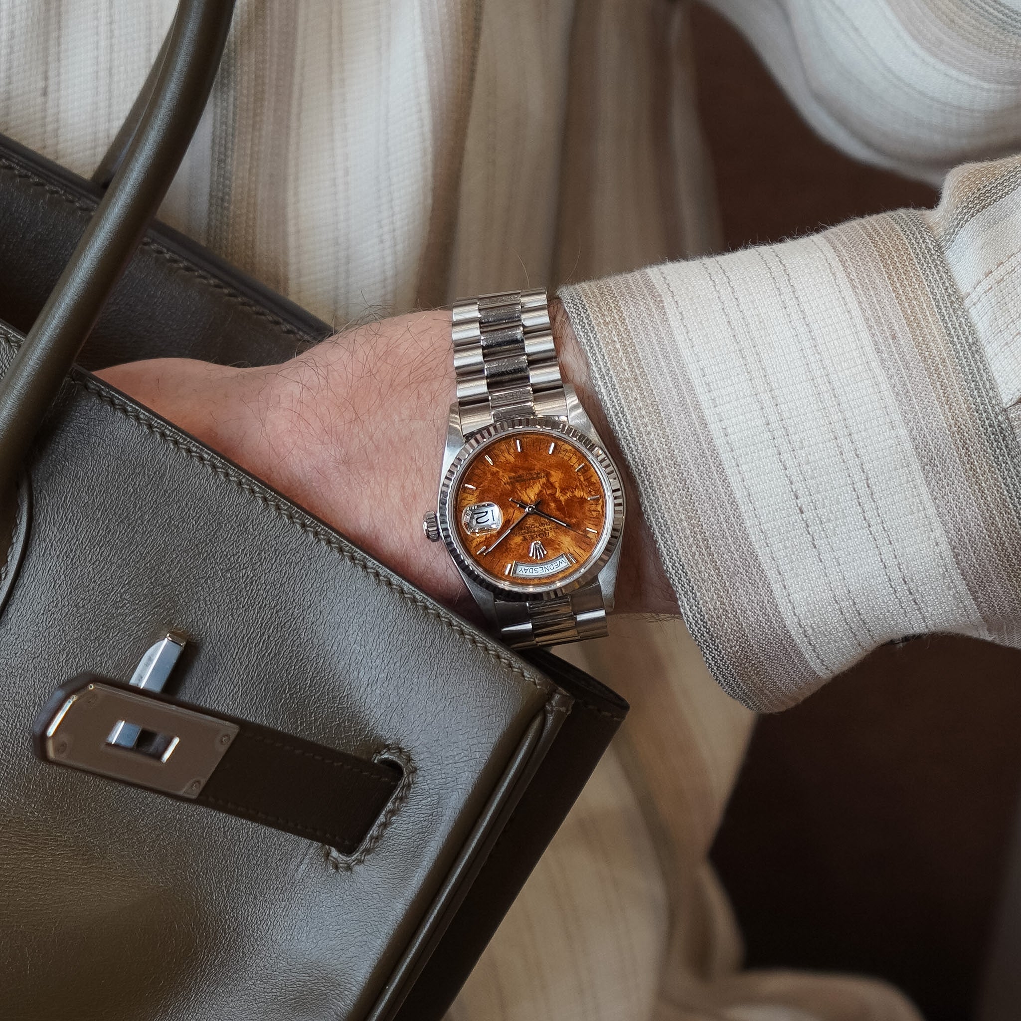 Person wearing a silver watch with an orange face, holding a brown leather handbag.