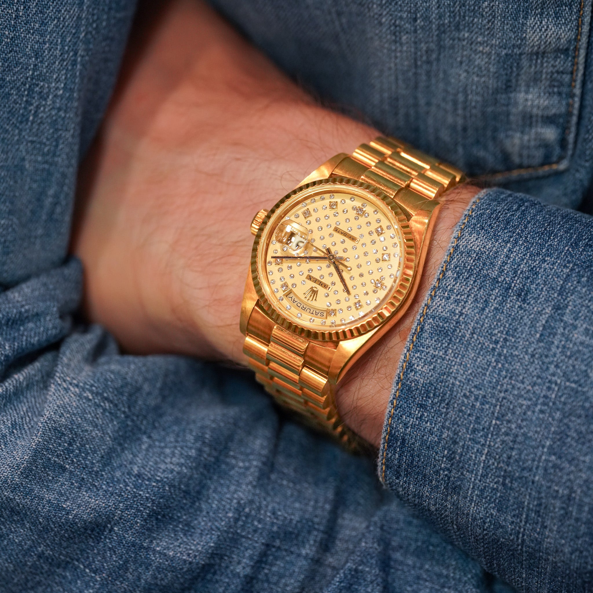 Gold watch on a person's wrist with a blue denim background