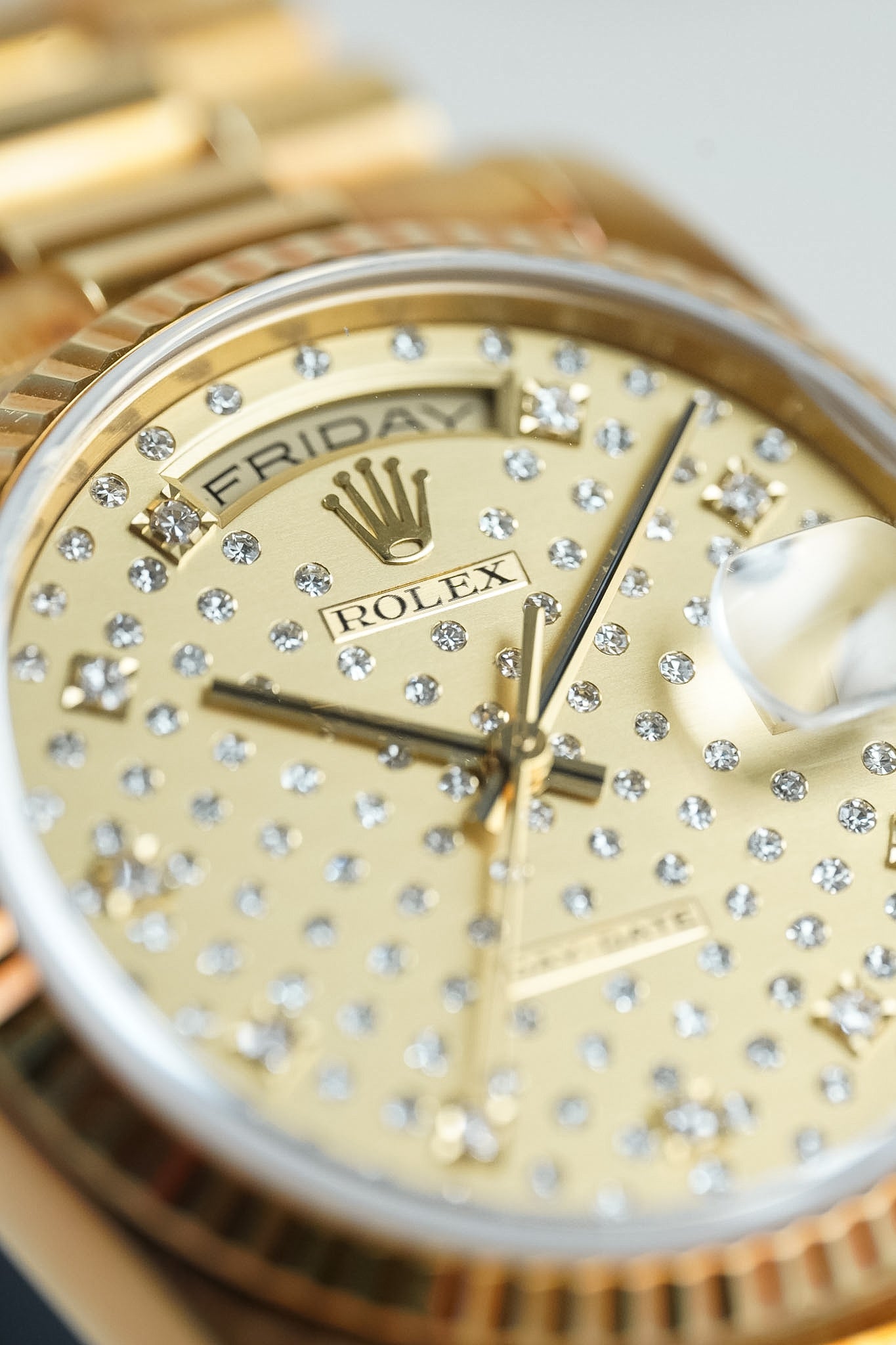 Gold Rolex watch with diamond-studded face on a light background