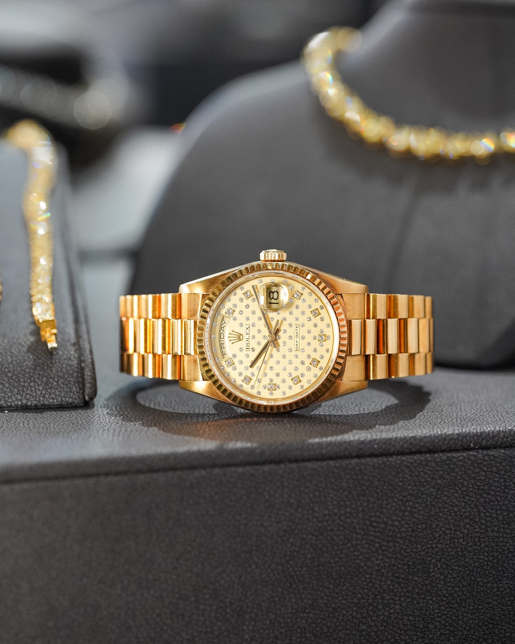 Gold watch on a black surface with blurred jewelry in the background