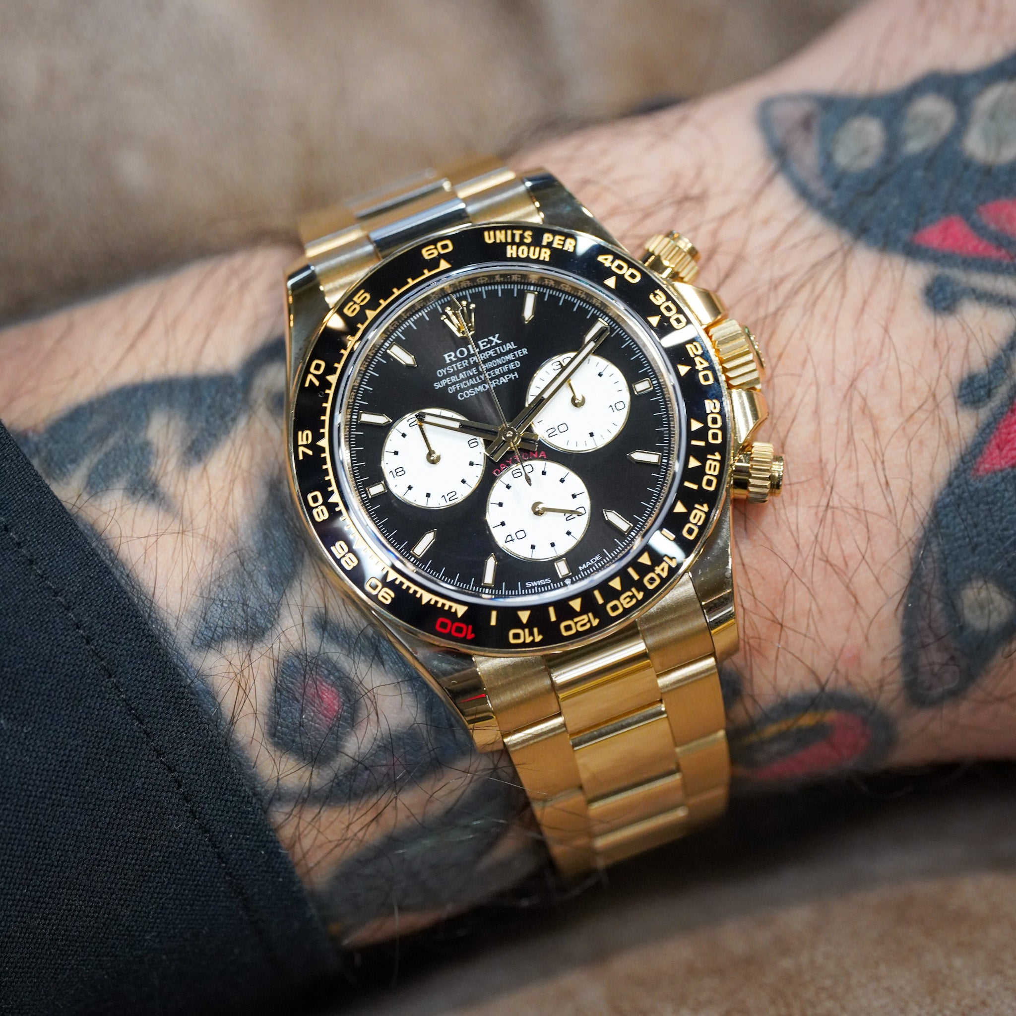Gold watch with black face on a wrist with tattoos