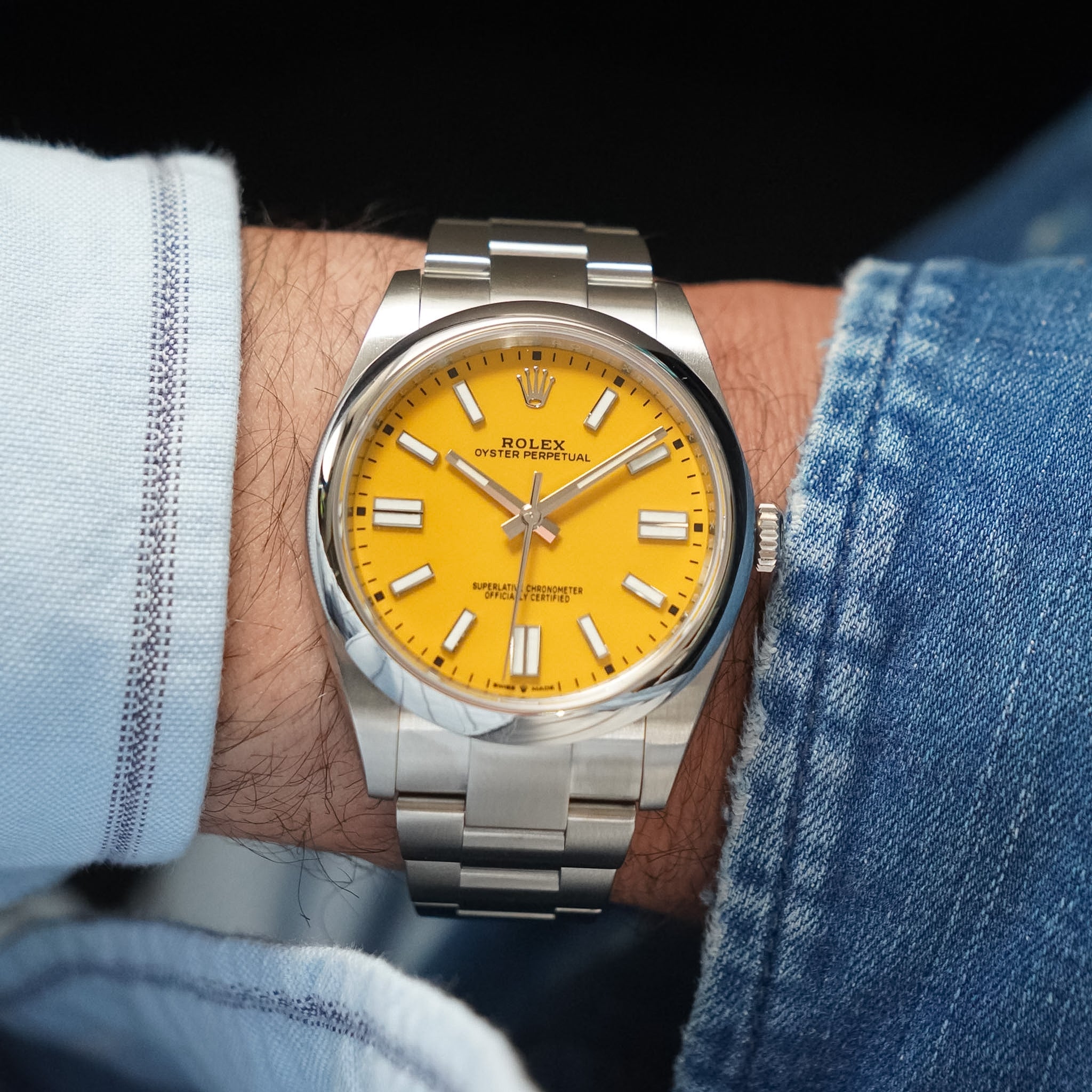 Rolex watch with yellow dial and silver case on a wrist, wearing denim jeans.