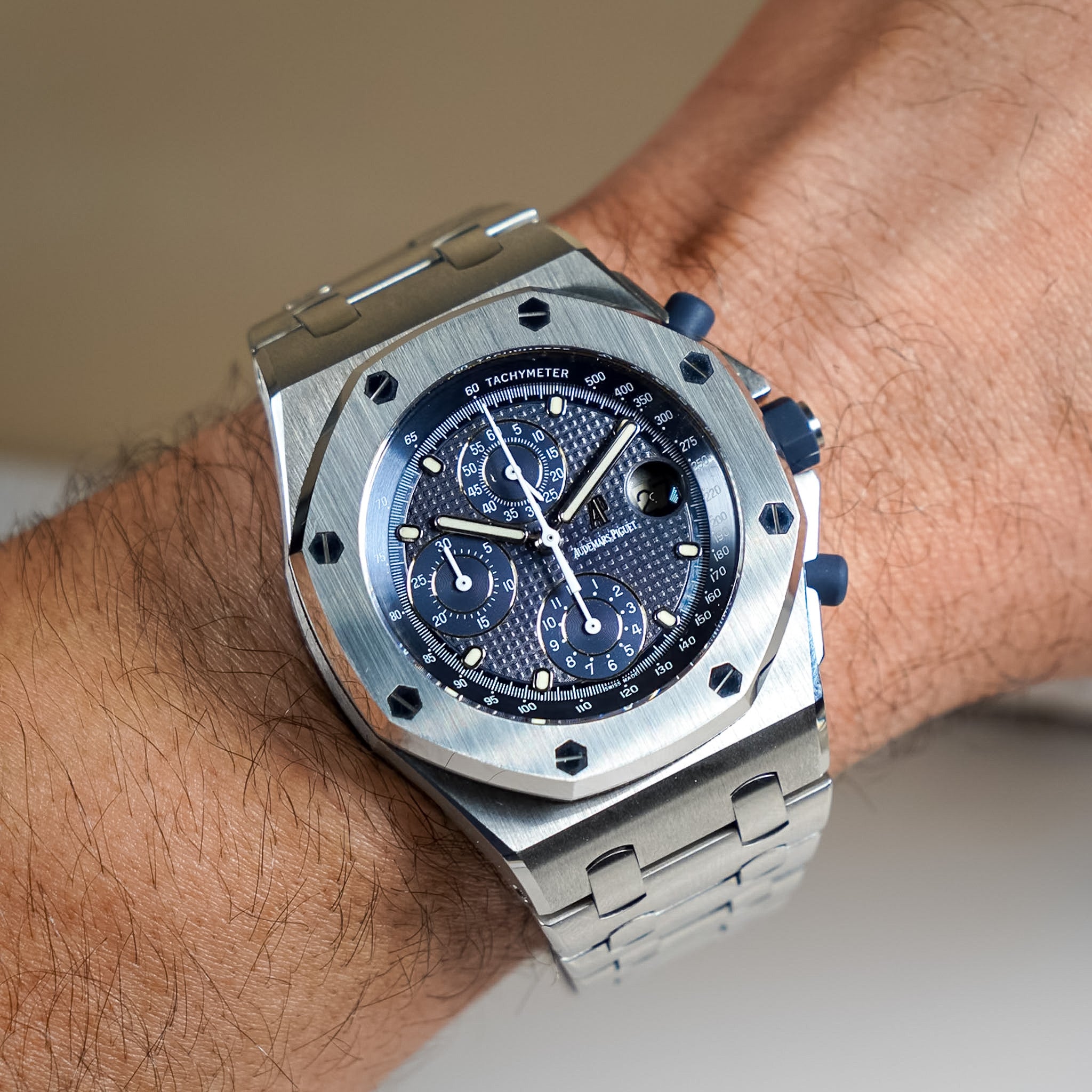 Silver watch with blue face on a wrist against a neutral background